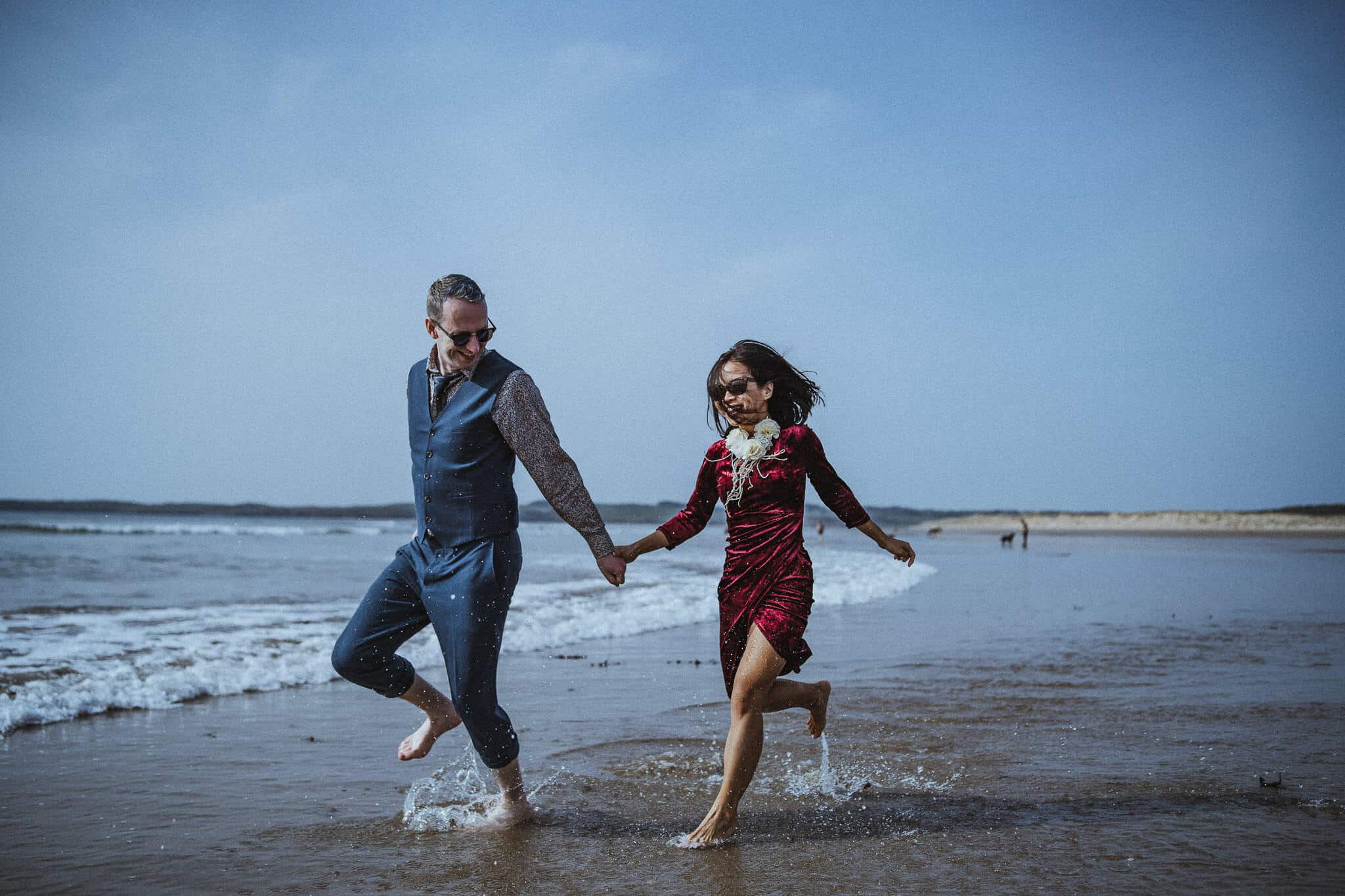 A couple running in the sea on Malltraeth Bay beach, Anglesey.